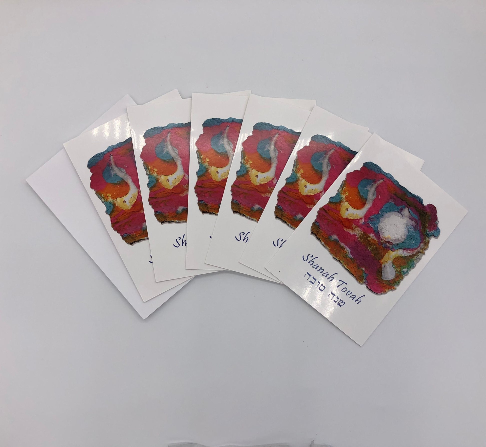 Six pack of graphic cards depicting original artwork with teal, pink and orange tones with white shofars above blue writing with both English and Hebrew Shanah Tovah