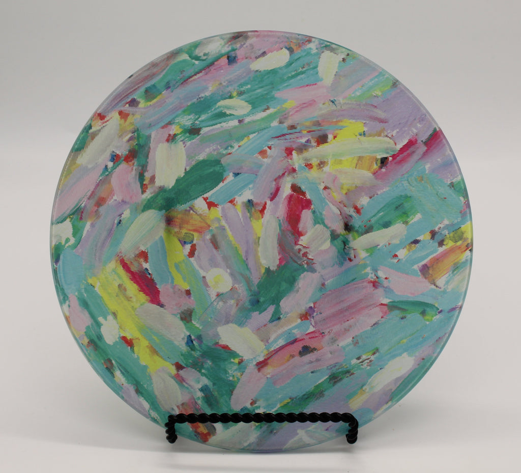 Circular glass cutting board depicting pink, turquoise, lavender, green and yellow paint streak design