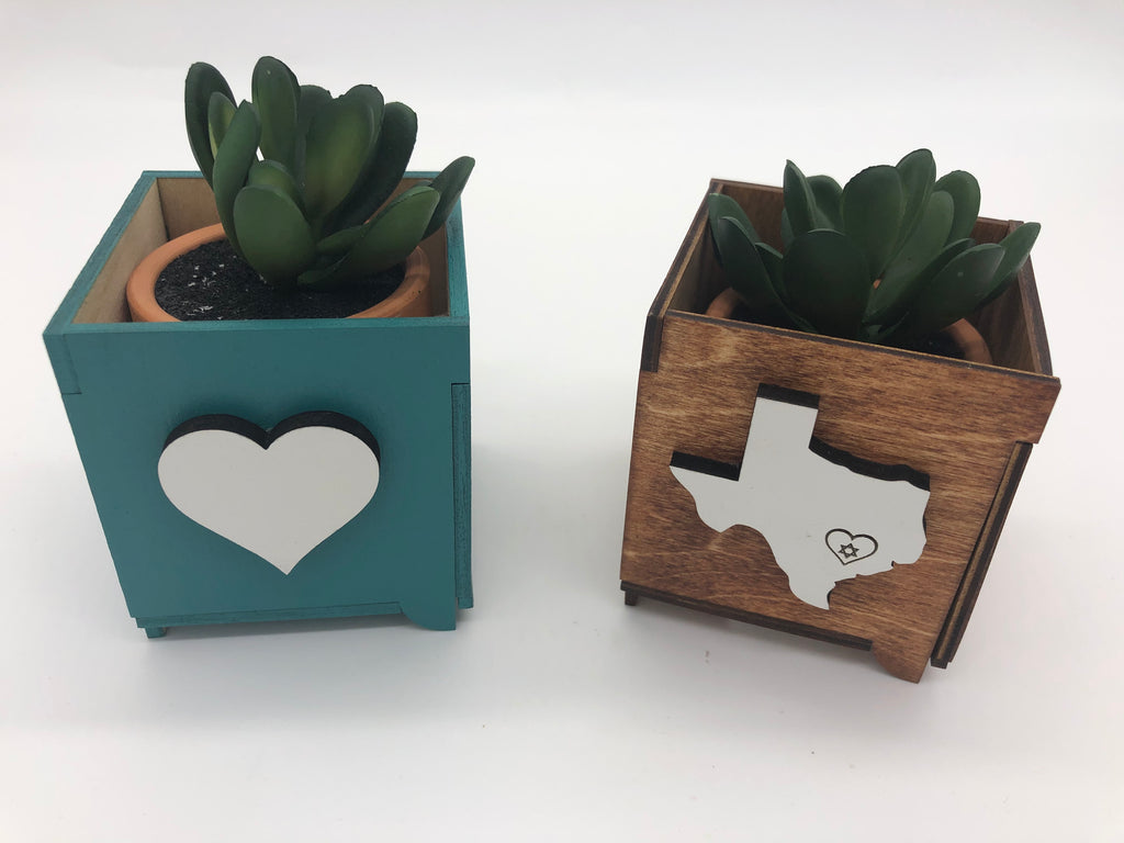 Two square wooden planters with small succulent plants in them.  The left planter is a light blue with a white heart.  The right planter is wood with a white Texas with a heart and Jewish star graphic over Houston