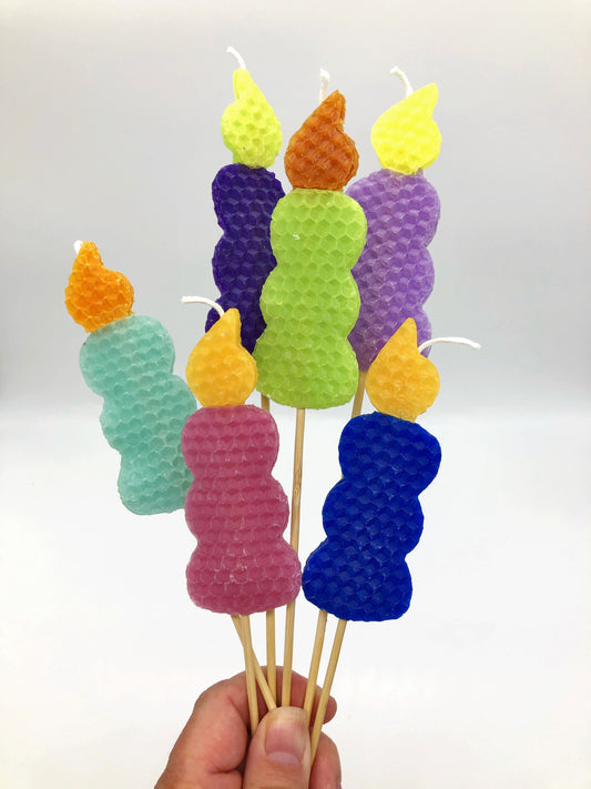 Beeswax candles in the shape of a candle with yellow and orange flames with blue, pink, green or purple bases