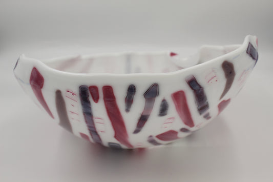 White glass fused bowl with lines of red, purple and brown