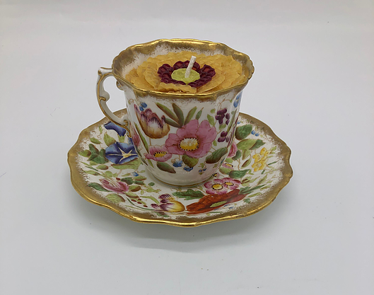 White teacup with a design of various colored flowers and a gold edge with a golden yellow candle inside