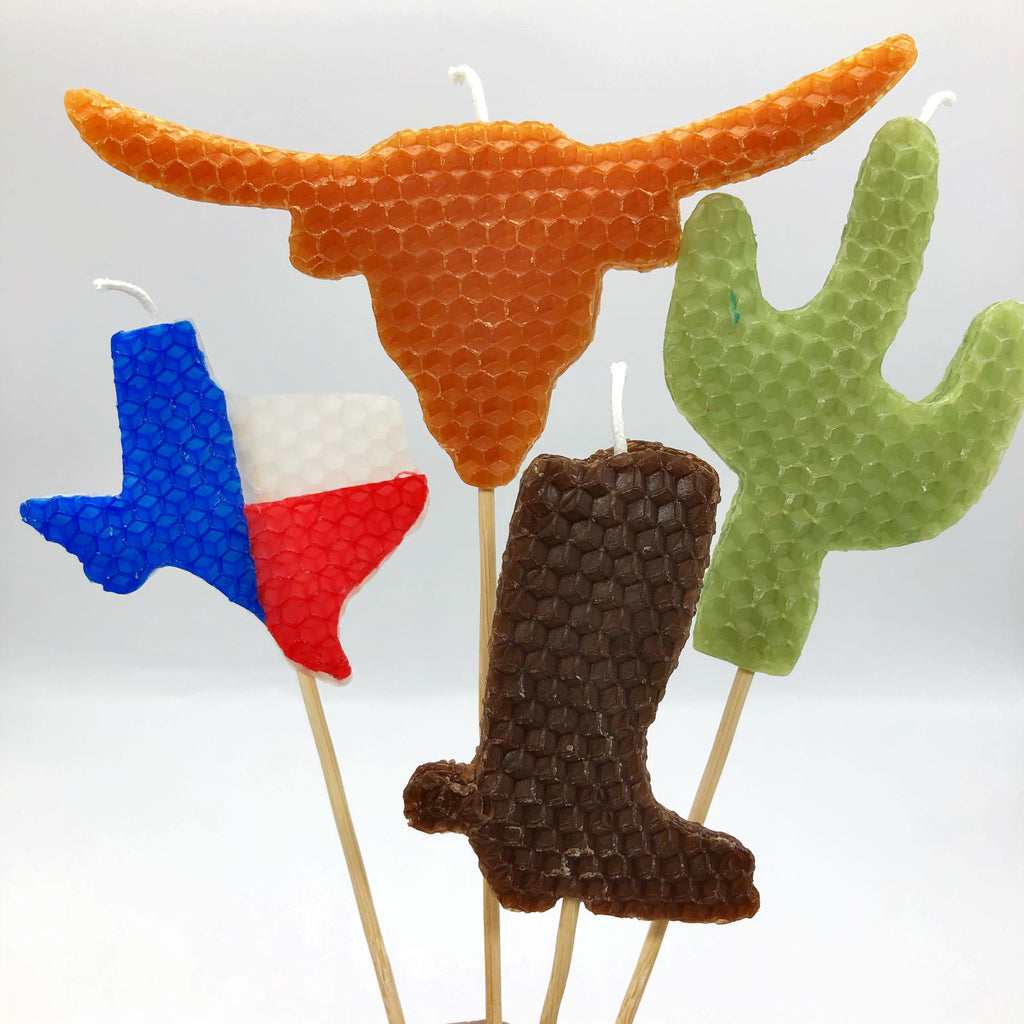 Large beeswax candles in the shape of Texas with the Texas flag, a burnt orange longhorn, a brown boot with spur, and a green cactus