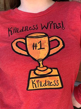 Close up view of red tshirt with black Kindness wins slogan above a trophy depicting a #1 and kindness on it