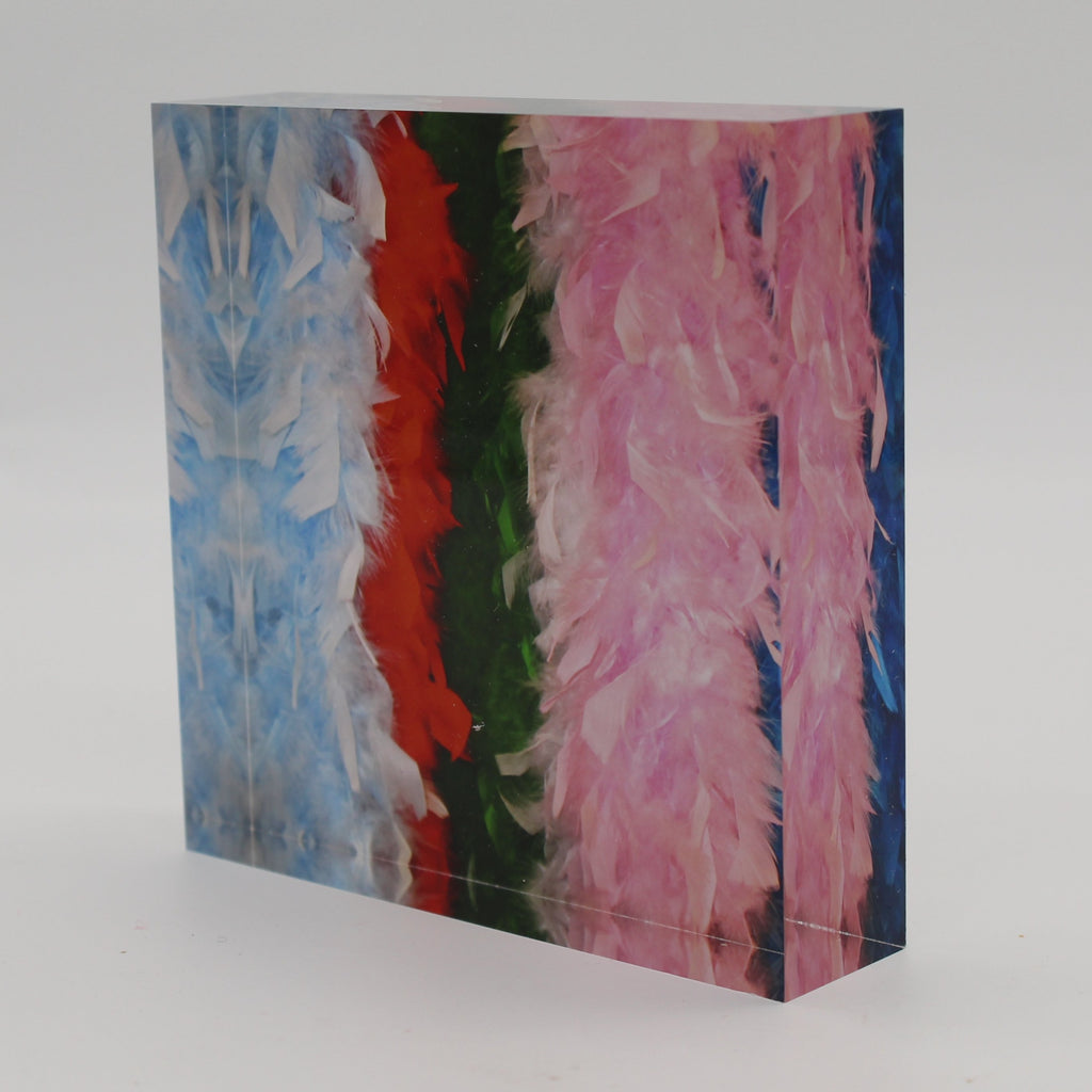 Tilted view of Acrylic block picture of light blue, red, green, pink and dark blue feather boas