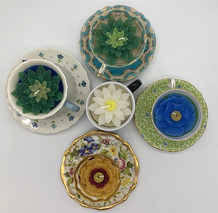 Various flower candles poured into tea cups sitting atop saucers