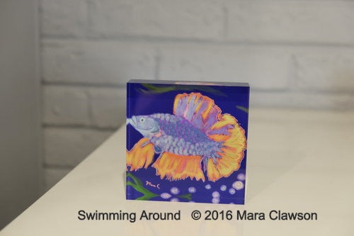 Acrylic block depicting a light blue fish with purplish scales and yellow and orange fins swimming in a blue ocean above bubbles and seaweed