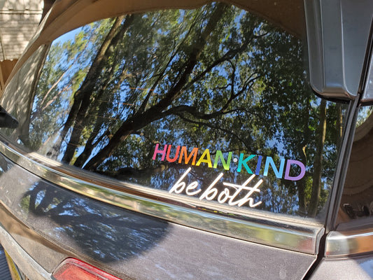 Windshield sticker with HUMAN KIND in rainbow colors and be both in white below
