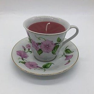 White teacup with purple flower print with gold edging with a deep red candle inside