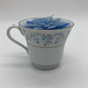 White tea cup with blue flower design and silver edge with a blue flower candle inside