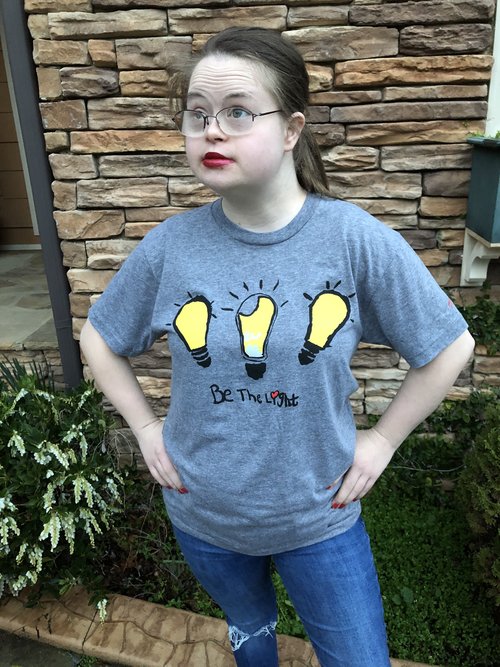 Young woman wearing gray tshirt with three yellow lightbulbs above Be The Light slogan