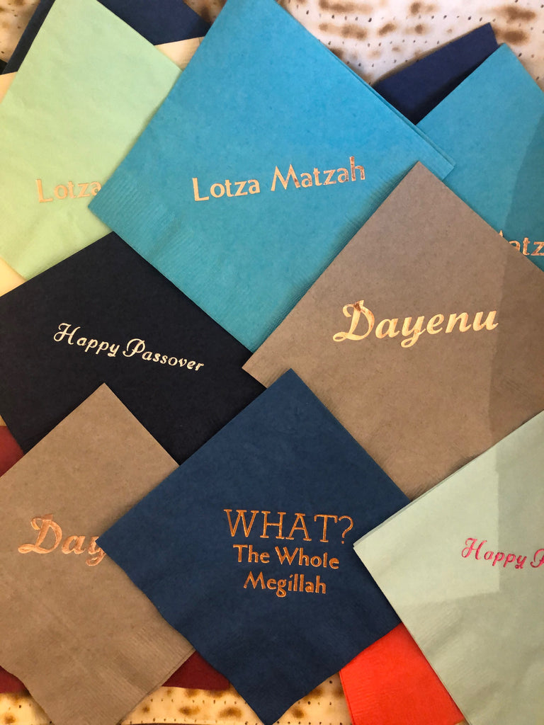 Various colored cocktail napkins with Passover slogans including Lotza Matzah, Happy Passover, Dayenu, and What? The Whole Megillah
