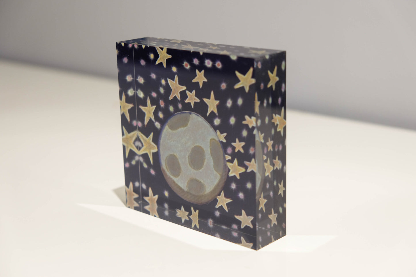 Tilted view of Acrylic block depicting outer space with a blue background and golden stars with Earth in the center