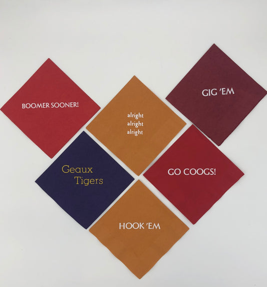 Varying colored napkins with college slogans including red napkin with Go Coogs! slogan, burnt orange napkins with Hook 'Em and alright, alright, alright slogans., purple napkin with gold Geaux Tigers slogan, red napkin with white Boomer Sooner! slogan, and maroon napkin with white Gig 'Em slogan