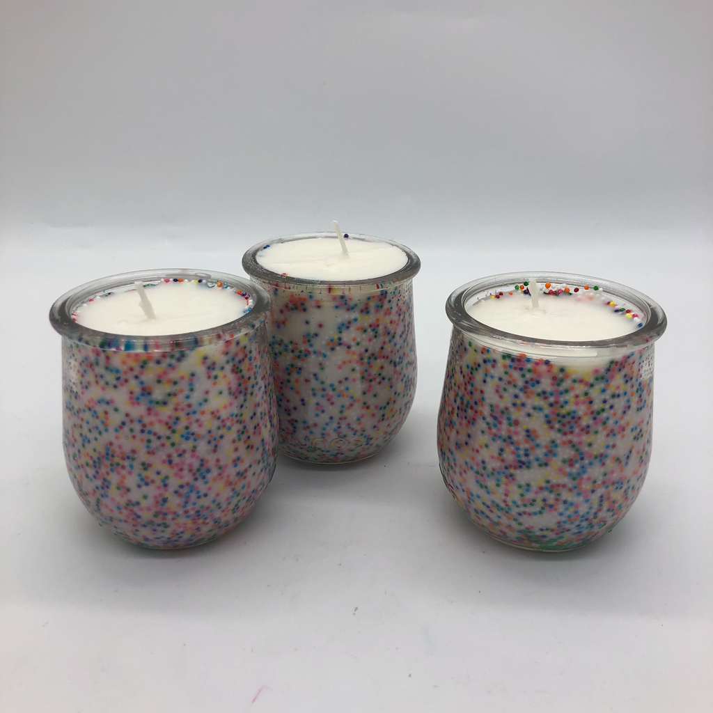 Three small glass jars with white candle inside. There are colorful sprinkles on the inside of the jars..