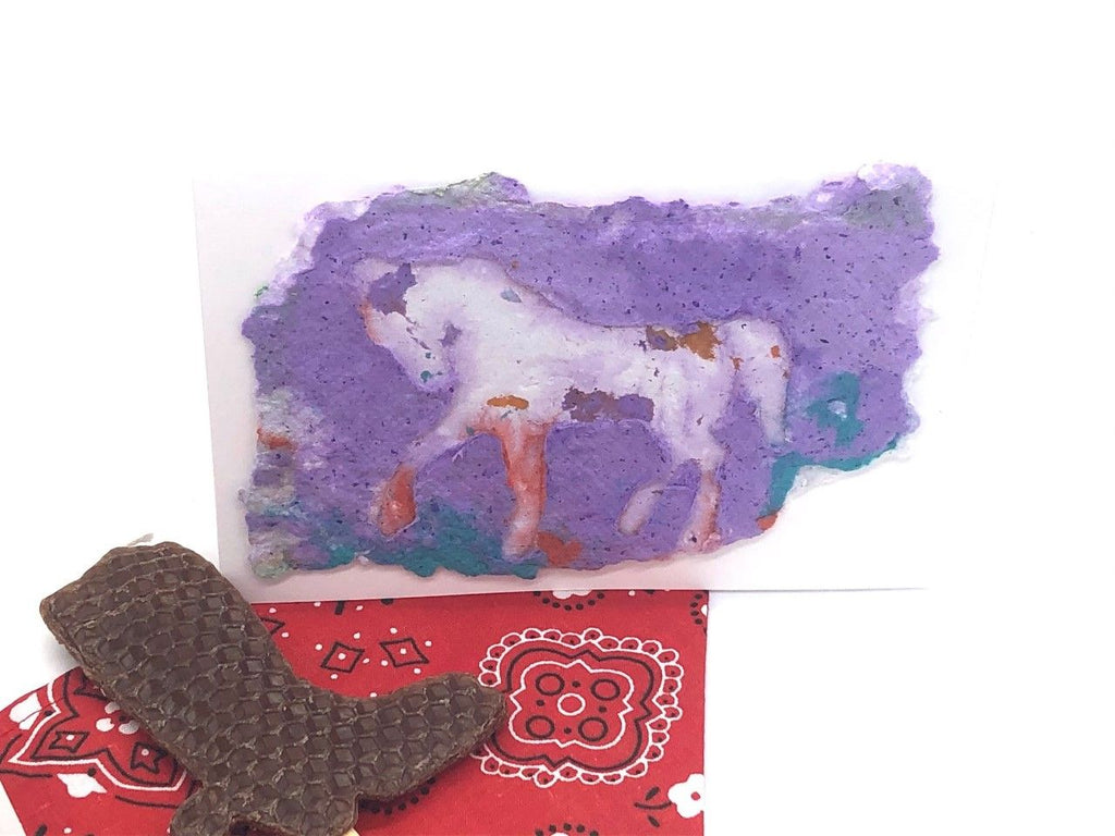 card with handmade paper design of a horse. vivid colors of purple, and blue. Red bandana and brown boot candle also displayed