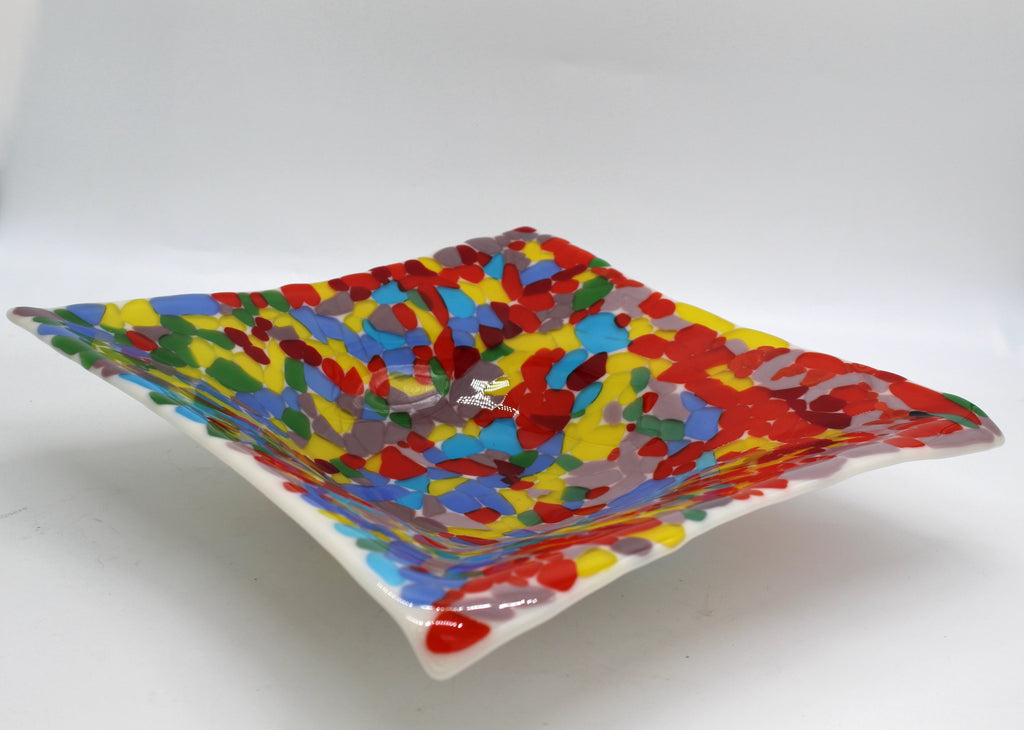 White glass square bowl completely covered in transparent chunks of bright colorful glass of reds, yellow, blues, green, and purple