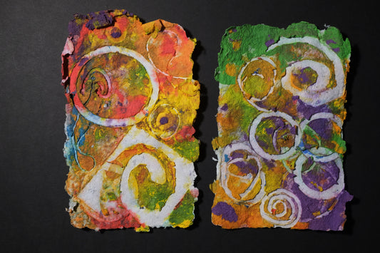 Two pieces of Pigment on recycled paper artwork with white circles and swirls against a background of yellows, greens and purples