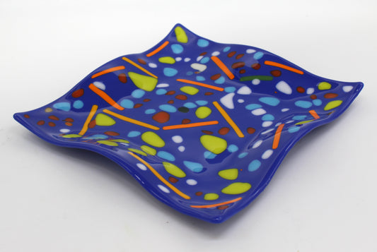 This is a piece of blue fused glass with multicolored dots and lines, including orange green white and red