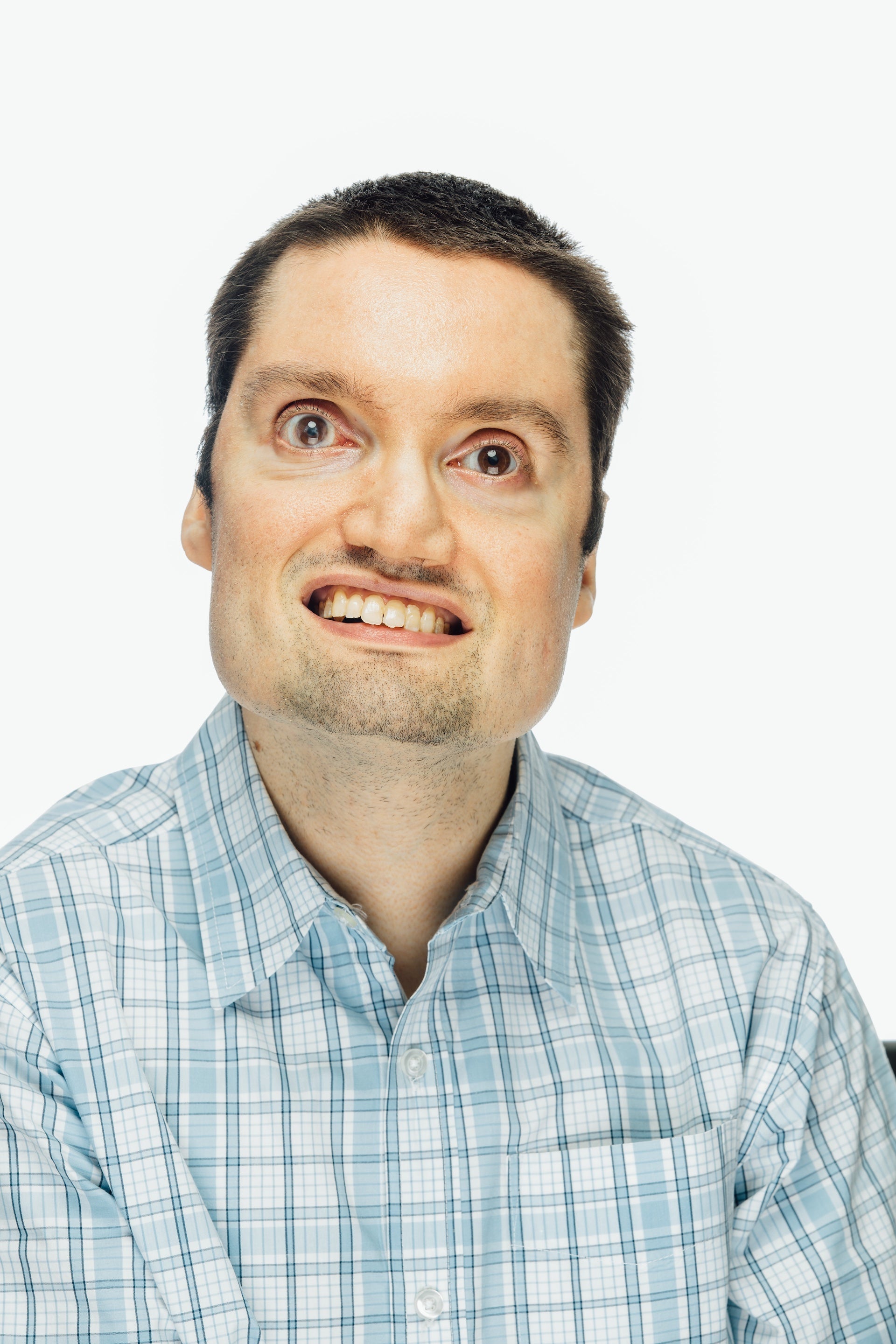 photograph of young man smiling with a buzz cut and is wearing a light blue plaid shirt