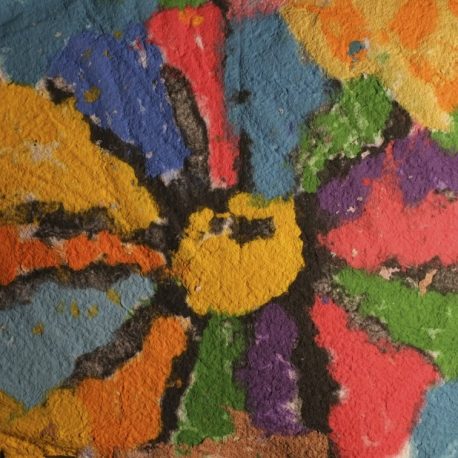 Pigment on recycled paper artwork of a large flower with yellow inside and blue, red, and green colored petals