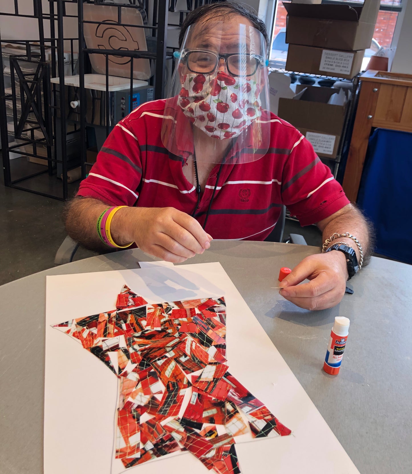 Participant with face mask and shield creating a piece of mosaic paper art.  Star of David is made from an orange photograph cut up.