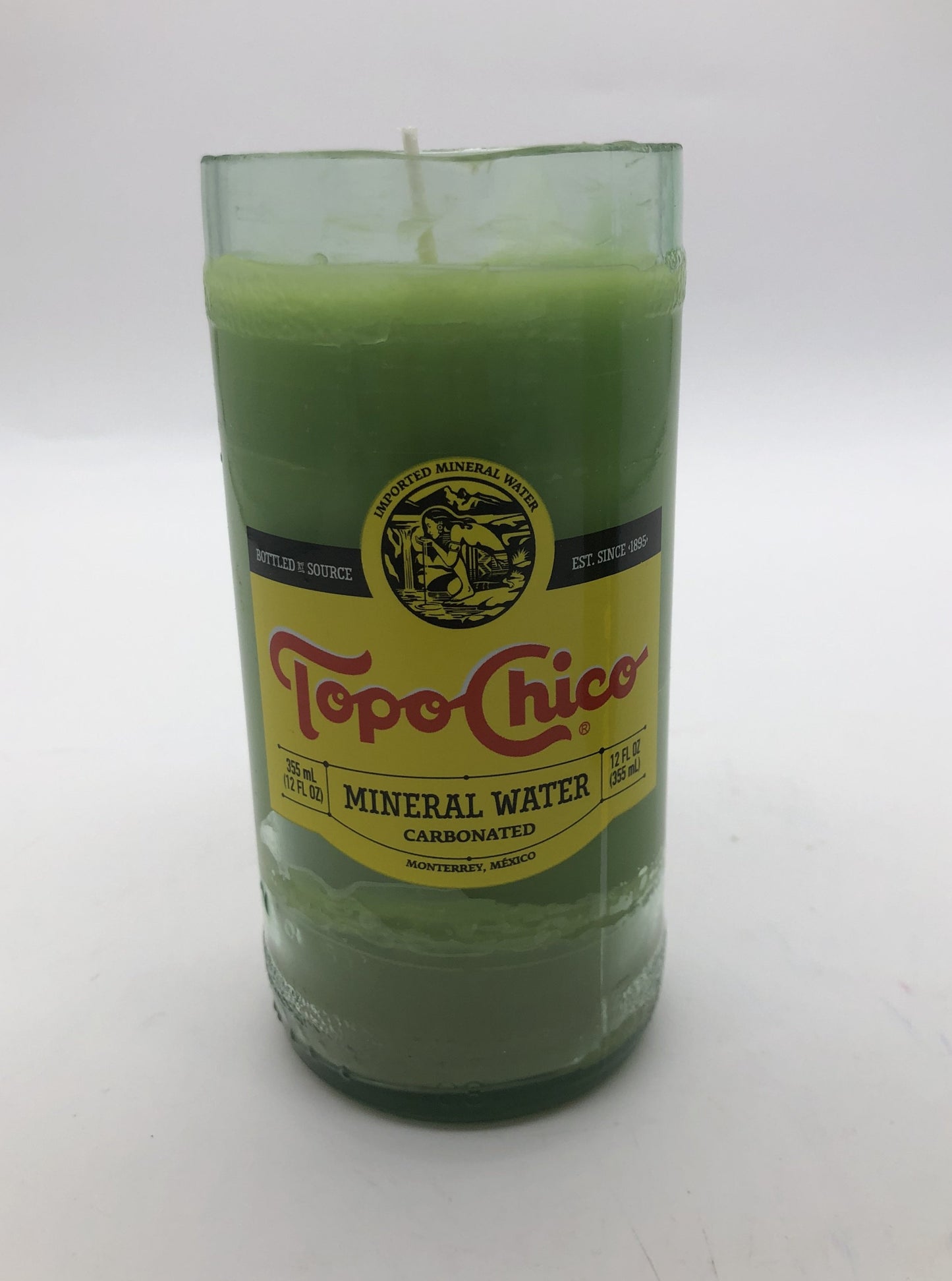 Cut clear bottle of Topo Chico with light green candle inside.