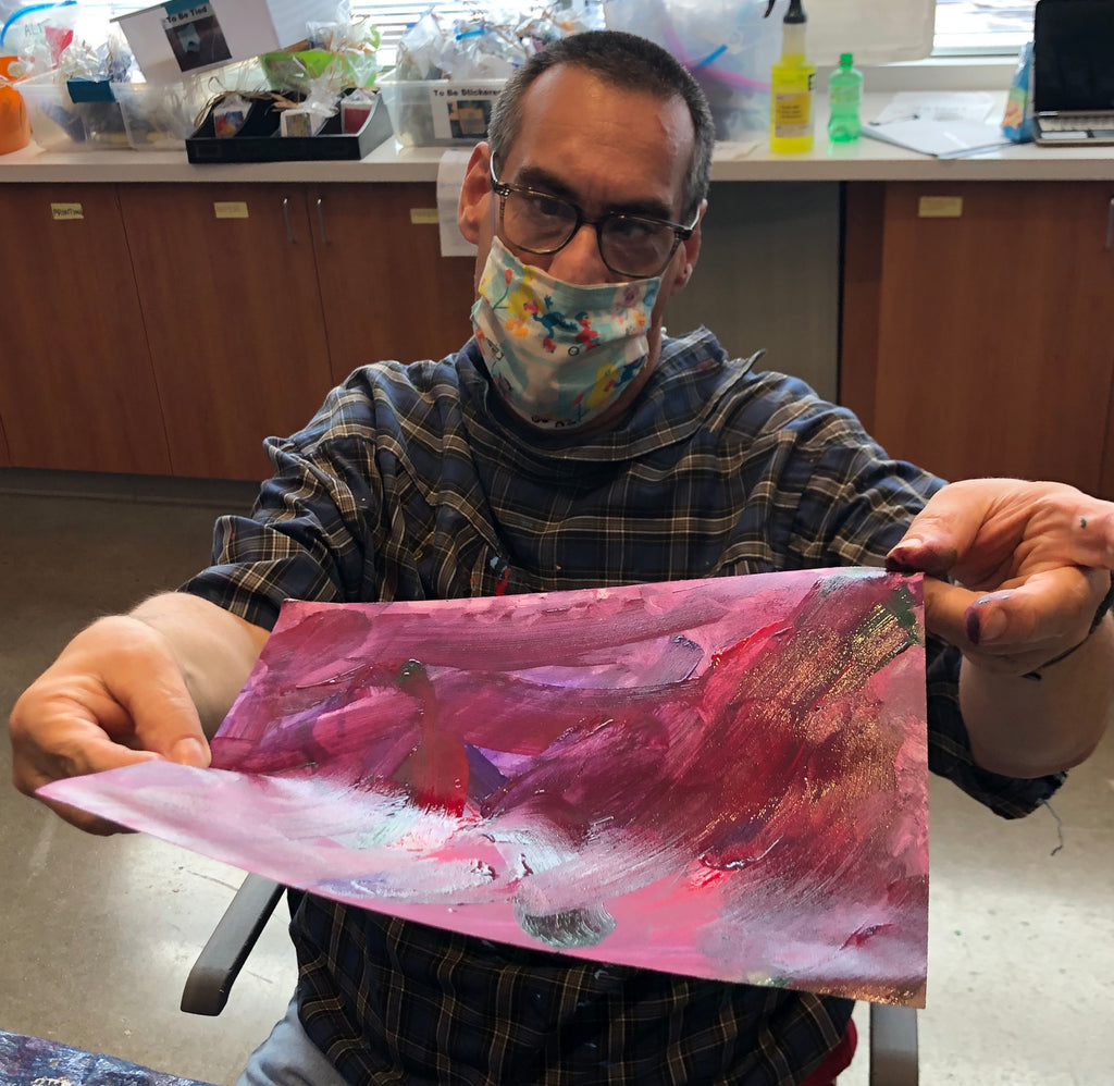 Male participant with a Seasame street mask holding a maroon and purple painting.