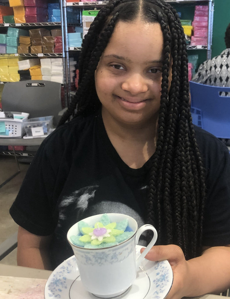 YOung woman with long dark braids on CC workfloor showing the teacup she decorated with a wax succulent.