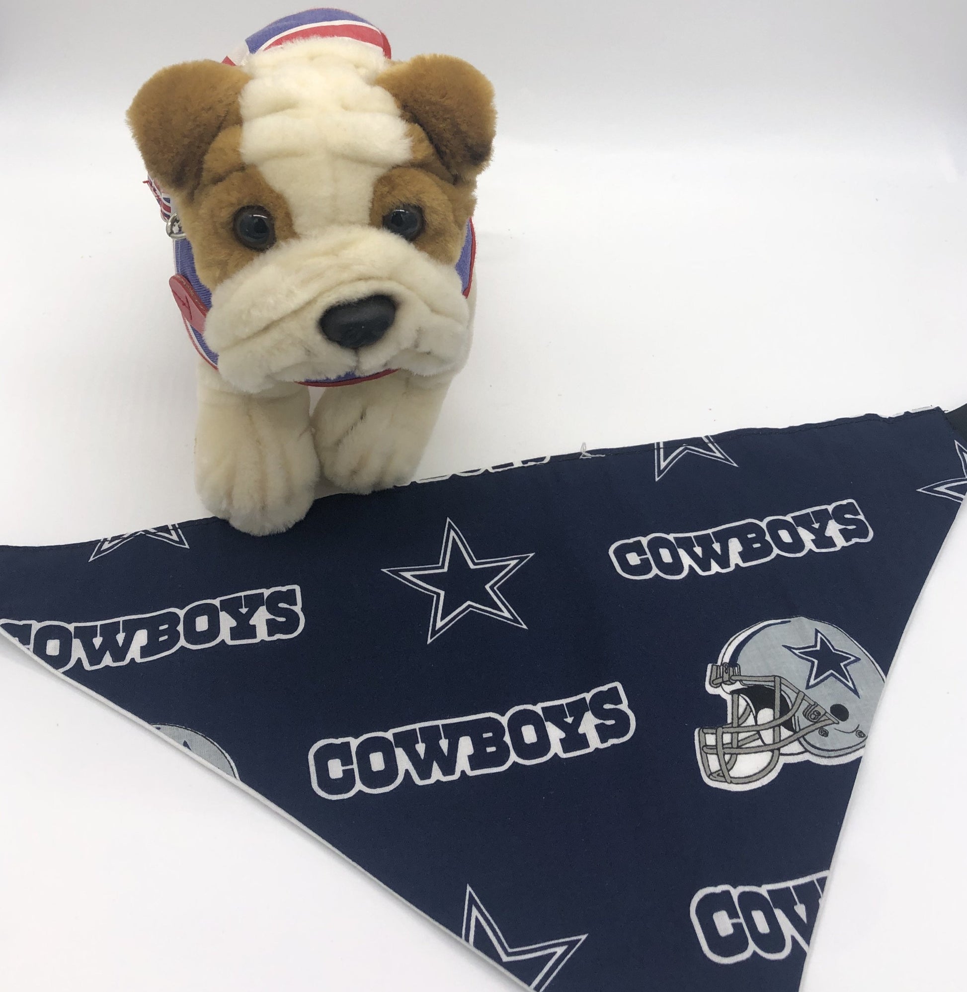 Photo of a small stuffed brown and cream dog standing by a Navy and grey triangular bandana with the Cowboys logo, star and helmet.