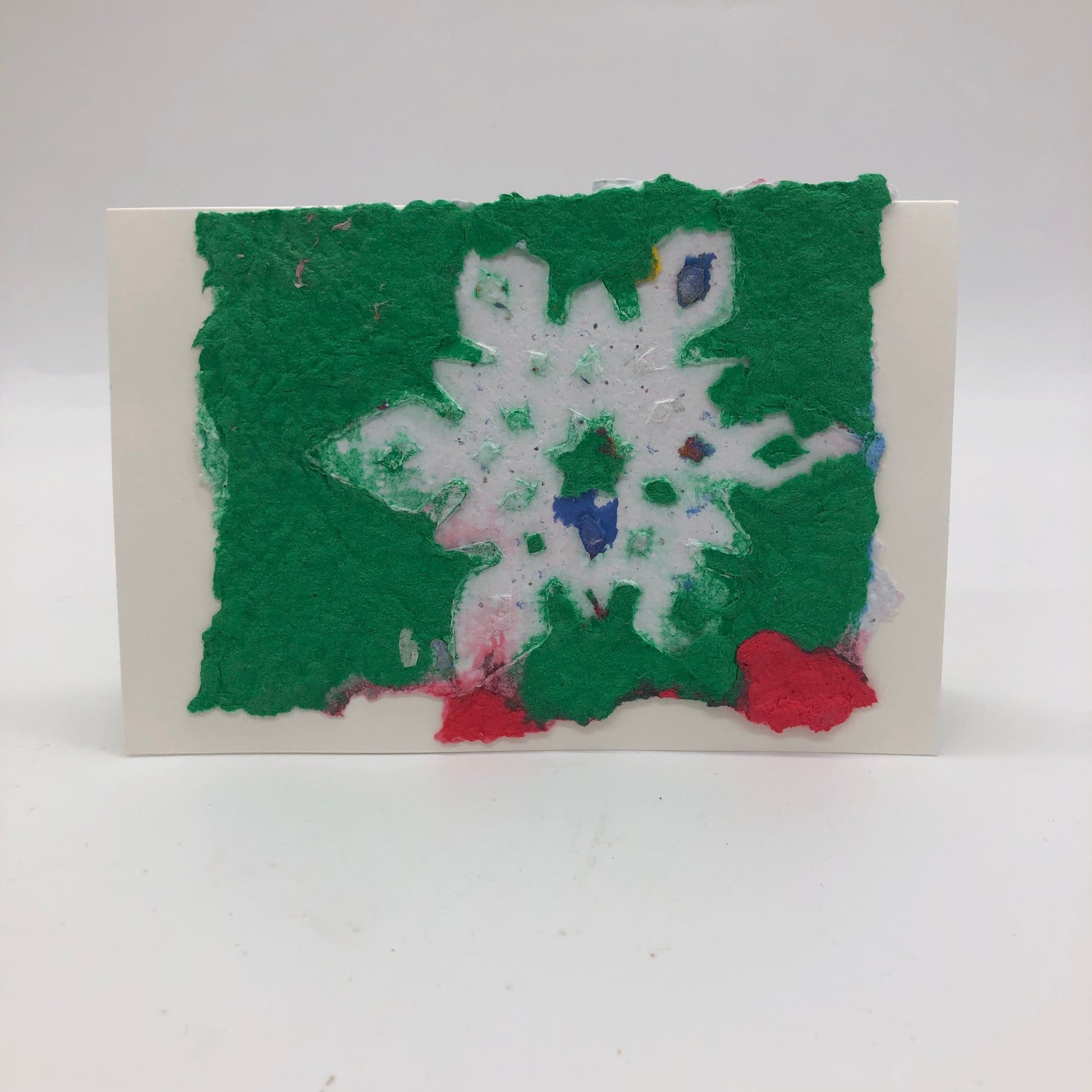 Handmade paper greeting card with green background with one large white snowflake and 2 blobs of red.