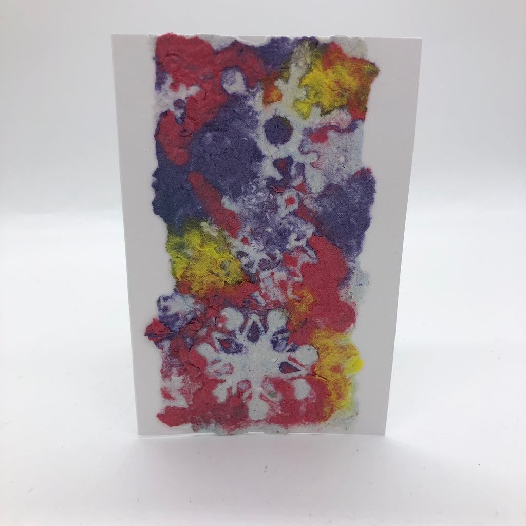 Handmade paper greeting card with pink, yellow and purple background with three white snowflakes