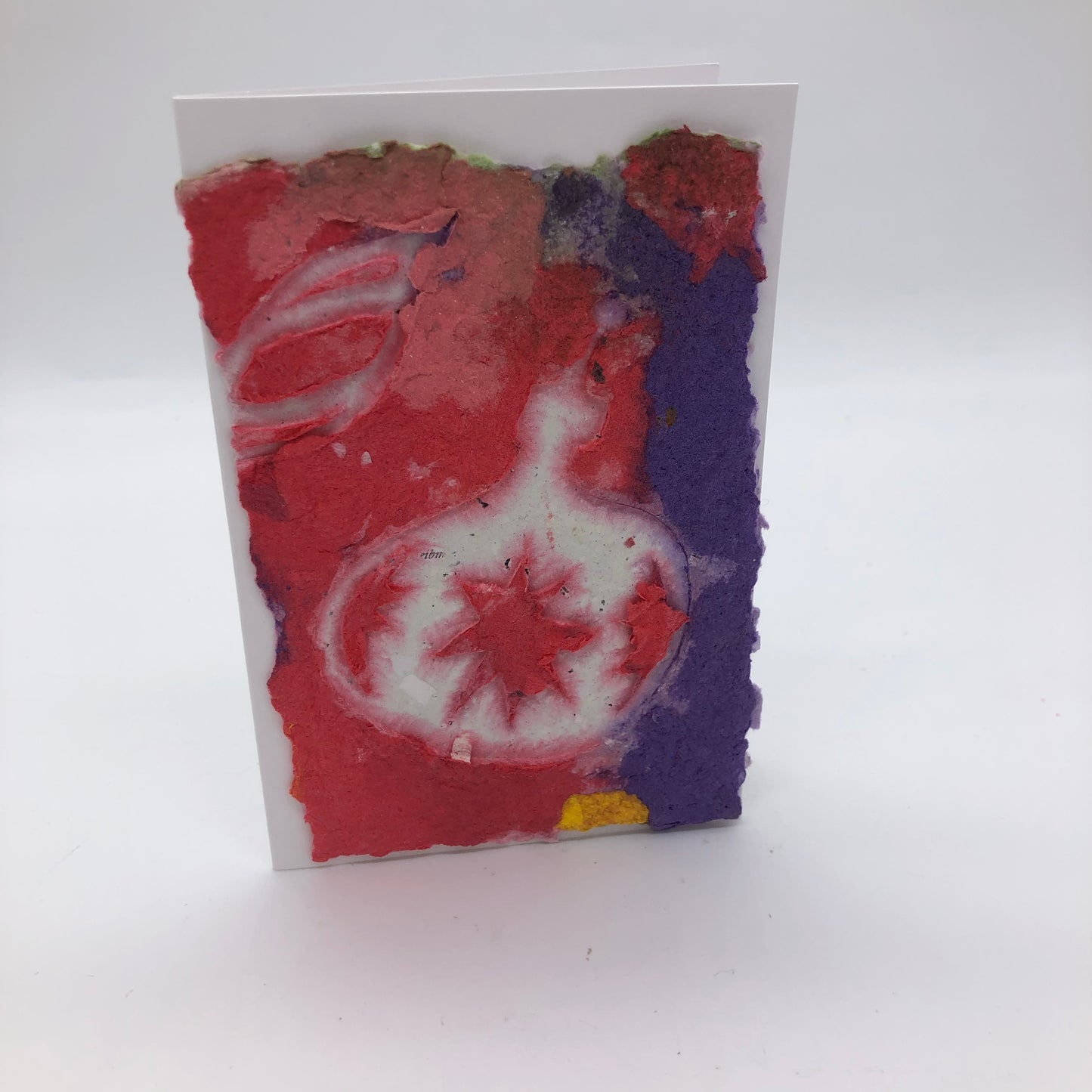 Handmade paper mostly in red and purple. There is one larger ornament with large starburst and two partial starburst.  There is a second partial pointy oval ornament at the top.  