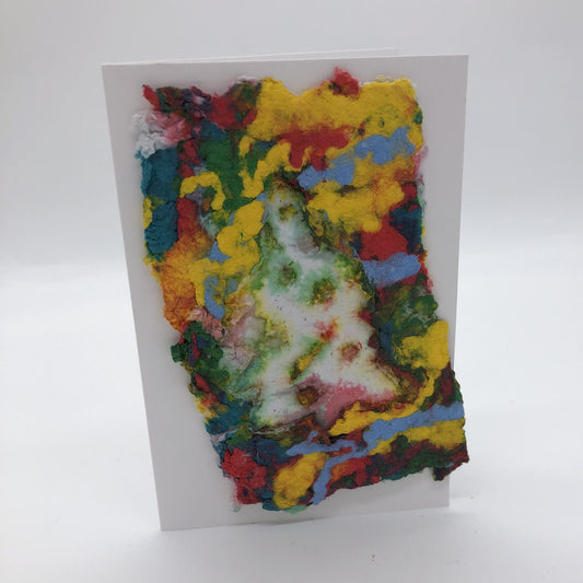 Handmade paper greeting card with several colors background, including yellow, red, blue, green and white Christmas tree.