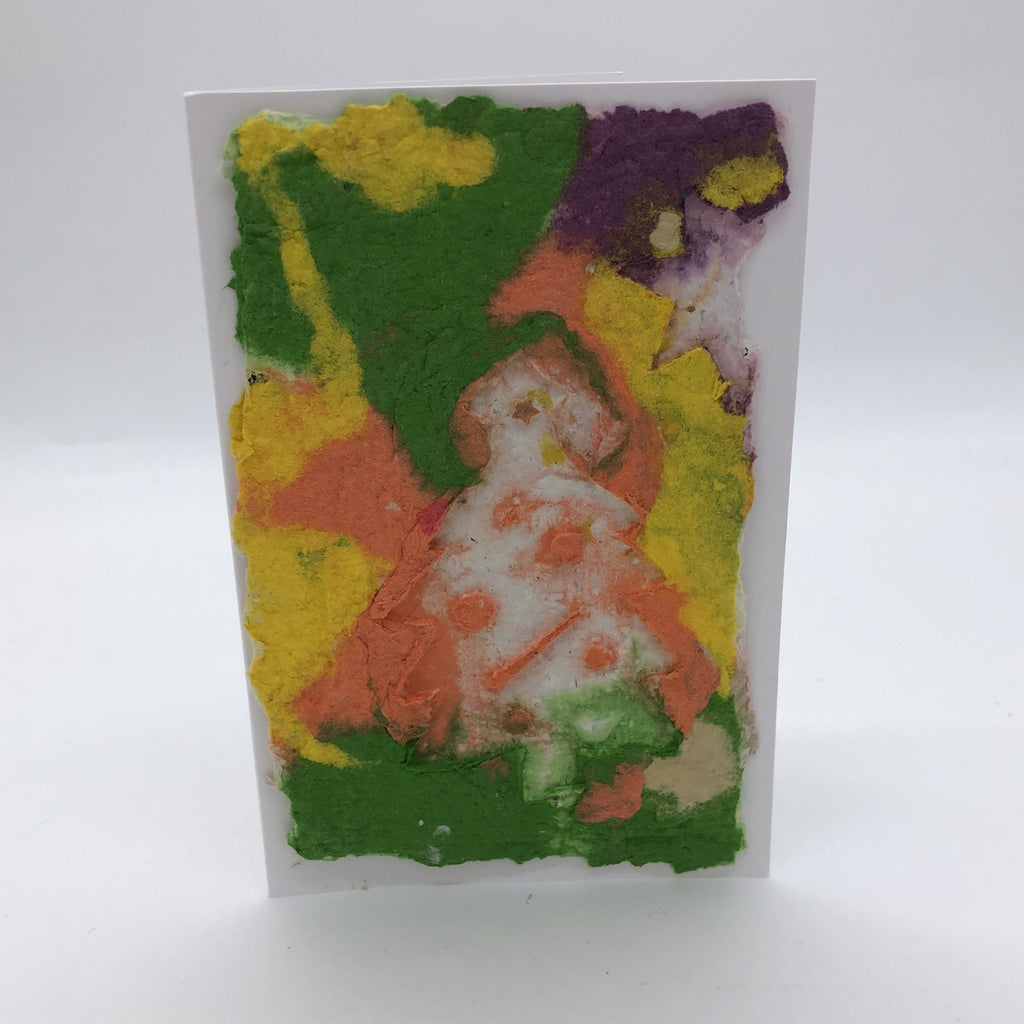 Handmade paper greeting card with green, peach, purple  and yellow background and white Christmas tree.
