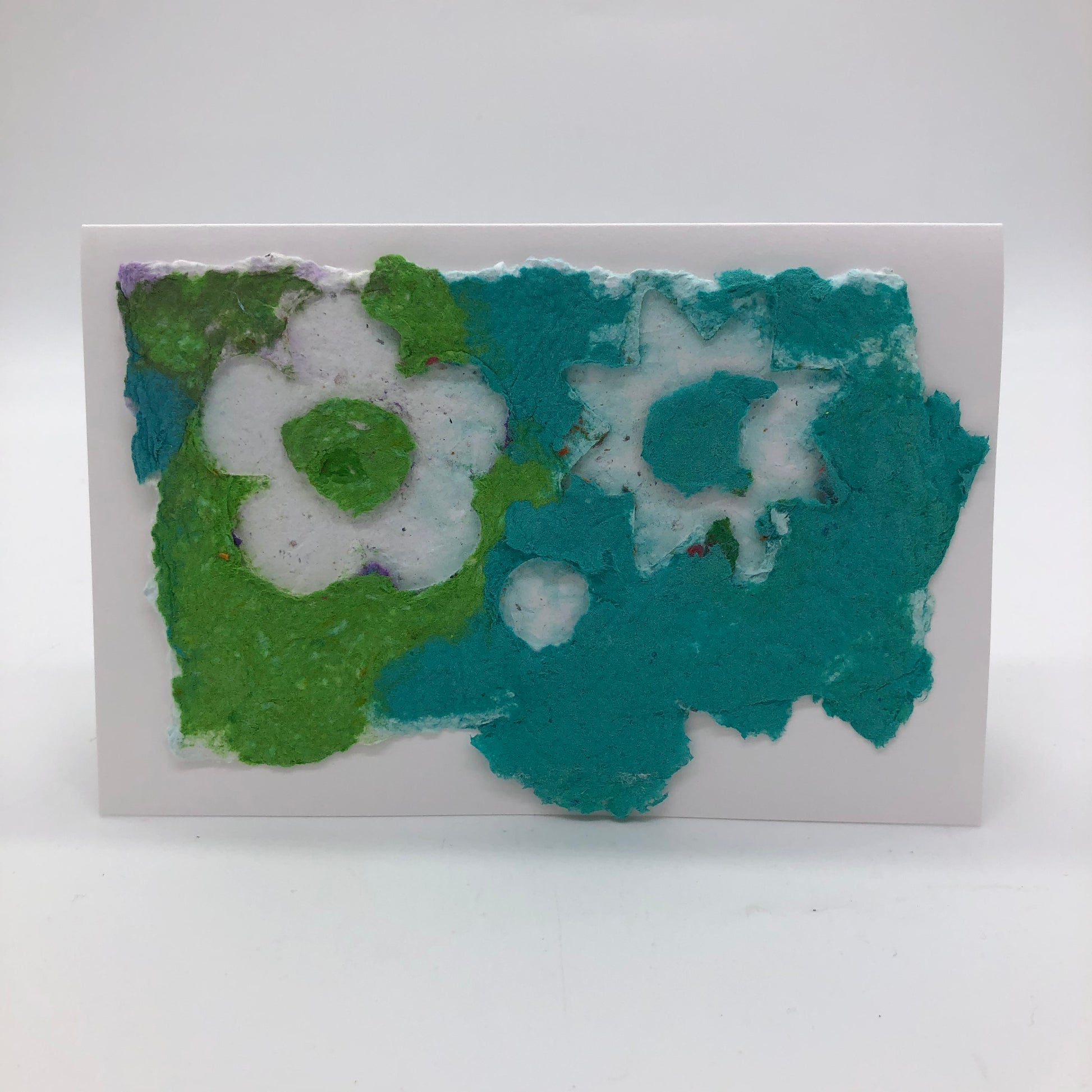 Horizontal greeting card made with handmade paper in bright green and teal.  Two cute flower shapes on top, both in white.  One flower has rounded petals, the other pointed petals.