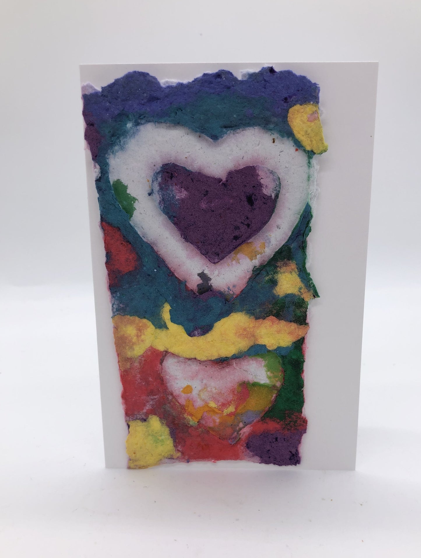 Handmade paper greeting card with blue, teal, yellow and red colors  in the background and a white and purpleheart