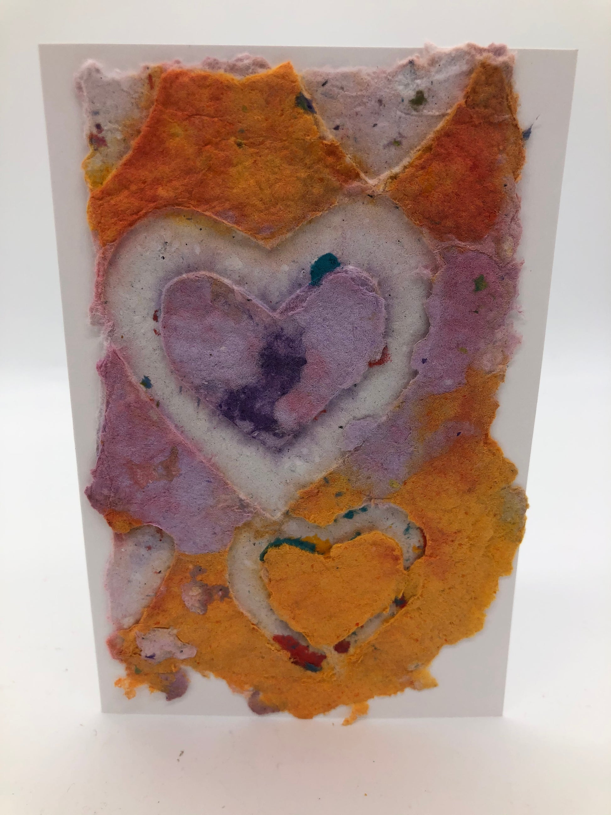 Handmade paper greeting card with purple, orange and lavender colors and a white heart with lavender heart inside itand yellow heart