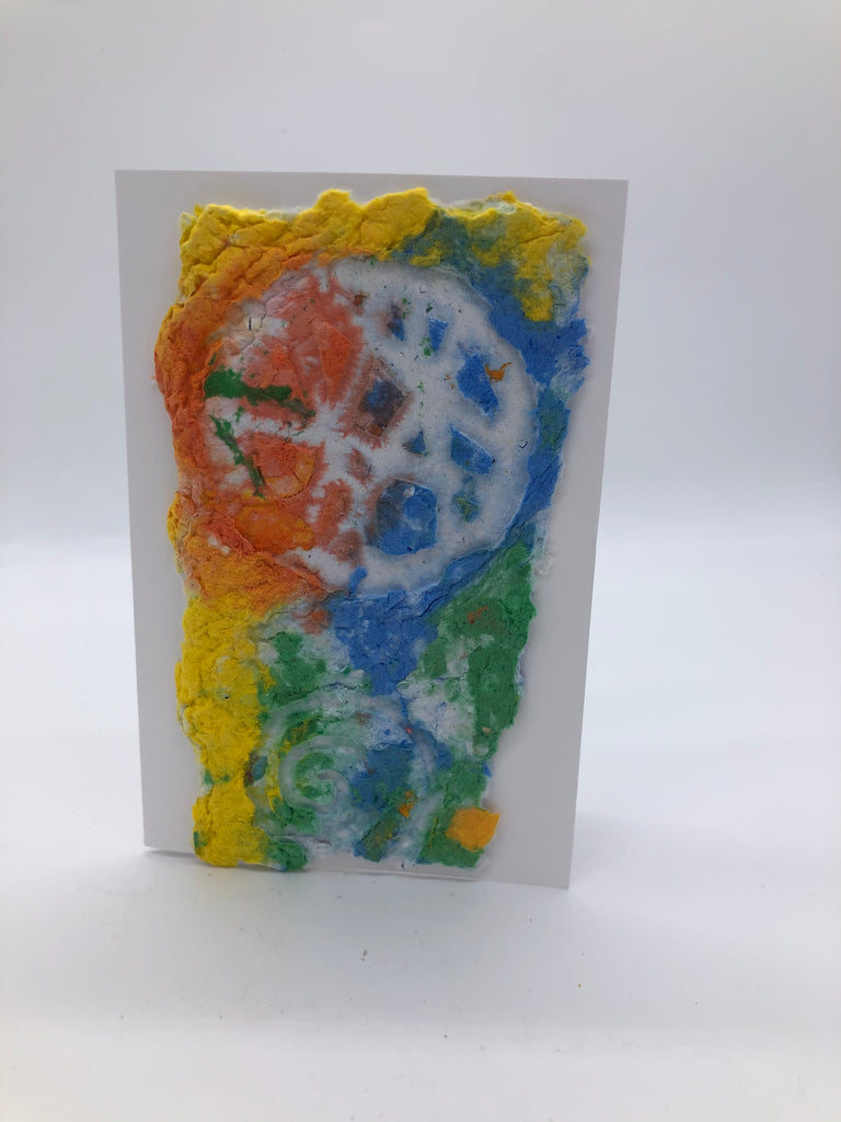 Handmade paper card in bright shades of yellow, orange blue and green.  The top portion has a white circle with many lines running through it.