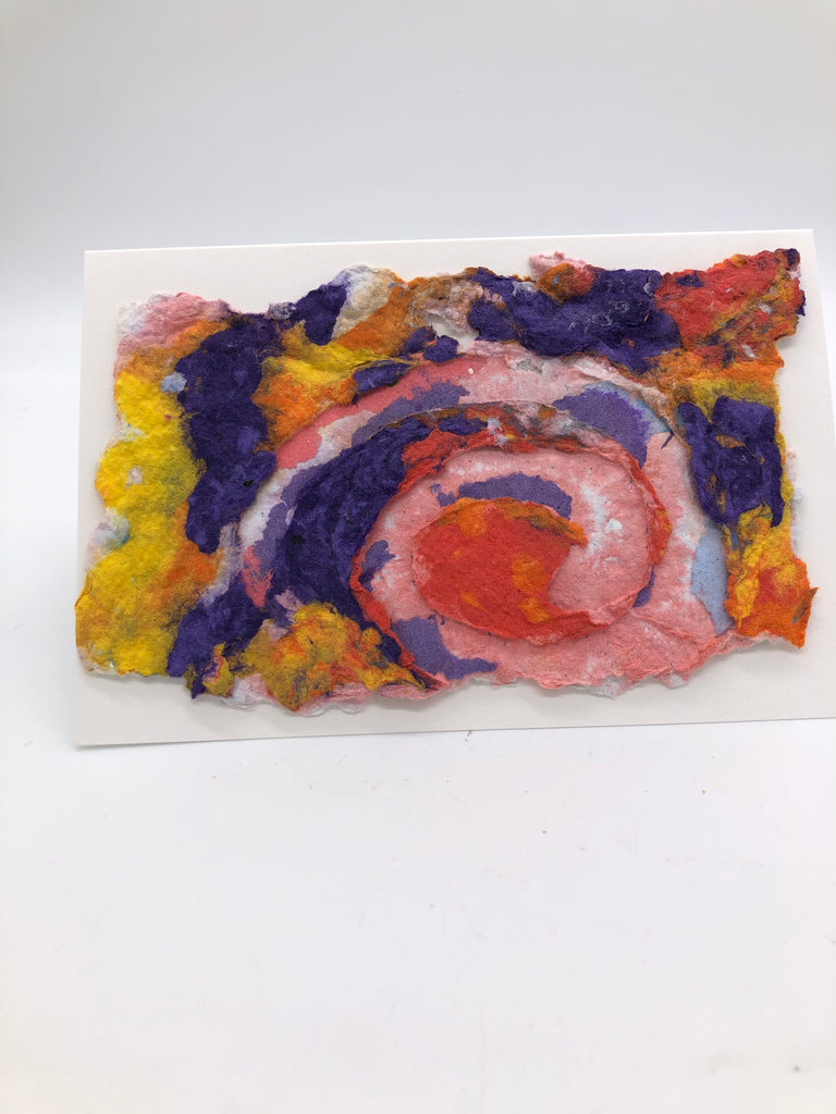 Handmade paper card with small patches of purple, yellow, orange and salmon.  On top is a large swirle with lighter shades of the background colors.