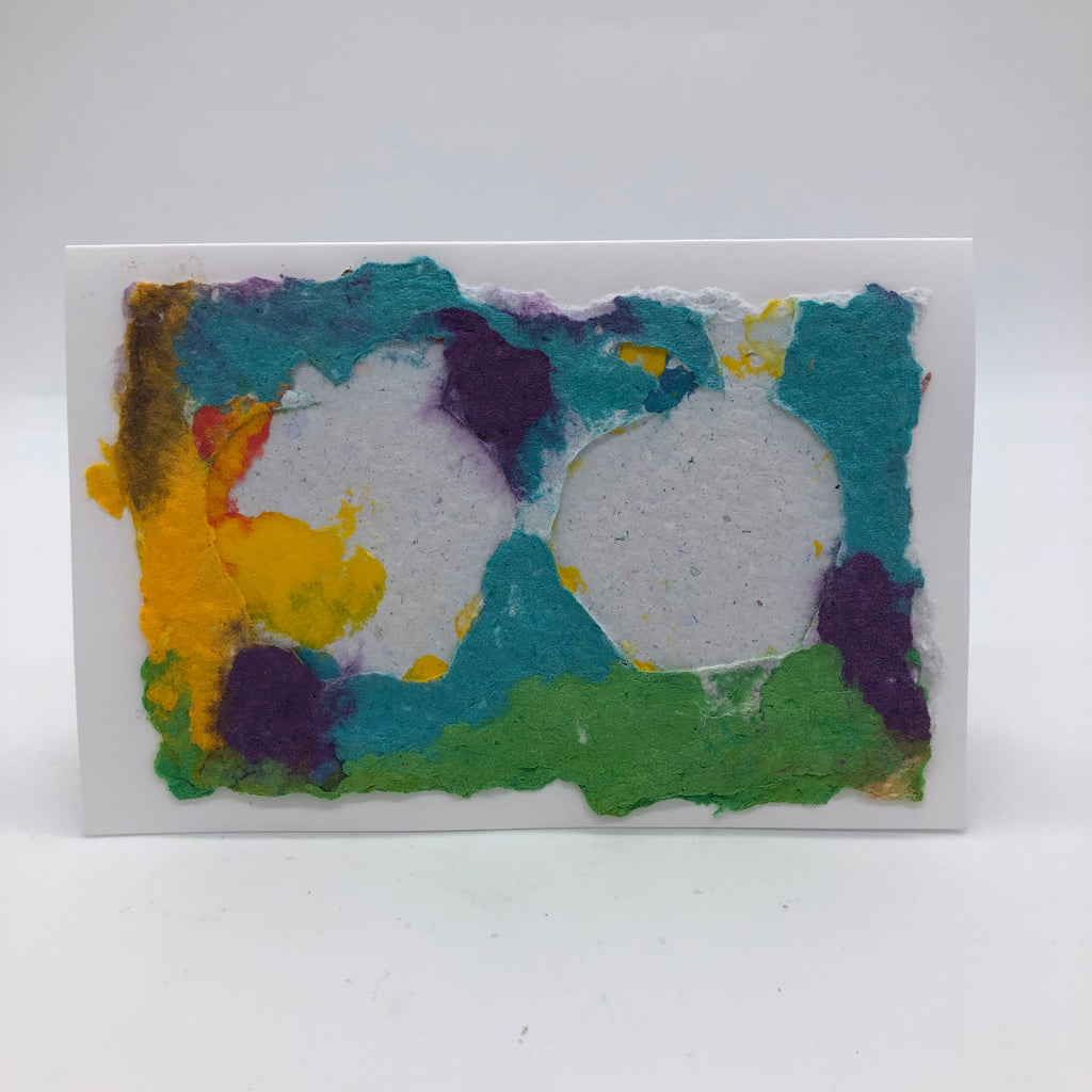 Handmade paper card with two apples in white on top of blue, teal, purple, yellow and green background.
