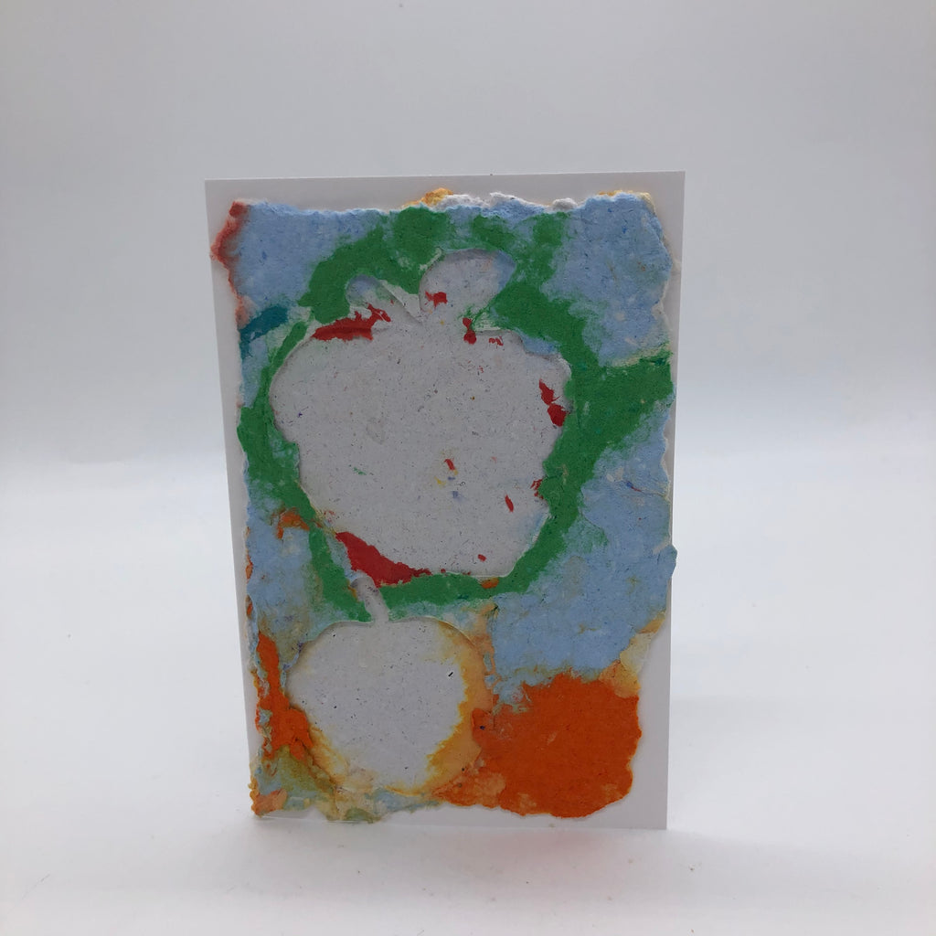 Handmade paper card with one large and one small apple in white.  THe background is light blue, medium blue and orange.