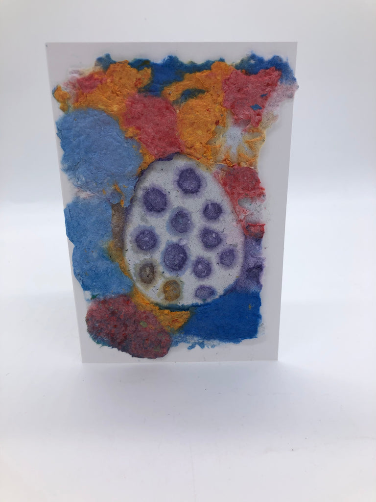 Handmade paper greeting card with shades of blues, orange, and red background with a  white Easter egg  with purple spots over top