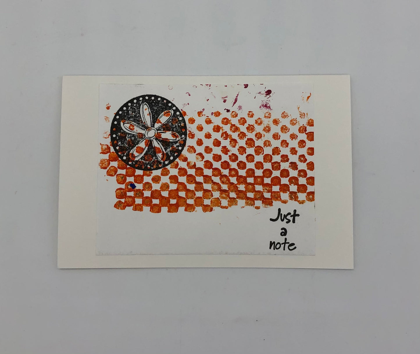 White greeting card with orange cirlces arranged in rows and columns with a freeform border at the bottom and left side.  On top of that is a circle stampe with a daisy in the middle.  This is on the upper left side. In the bottom right in black is stamped "Just a Note"