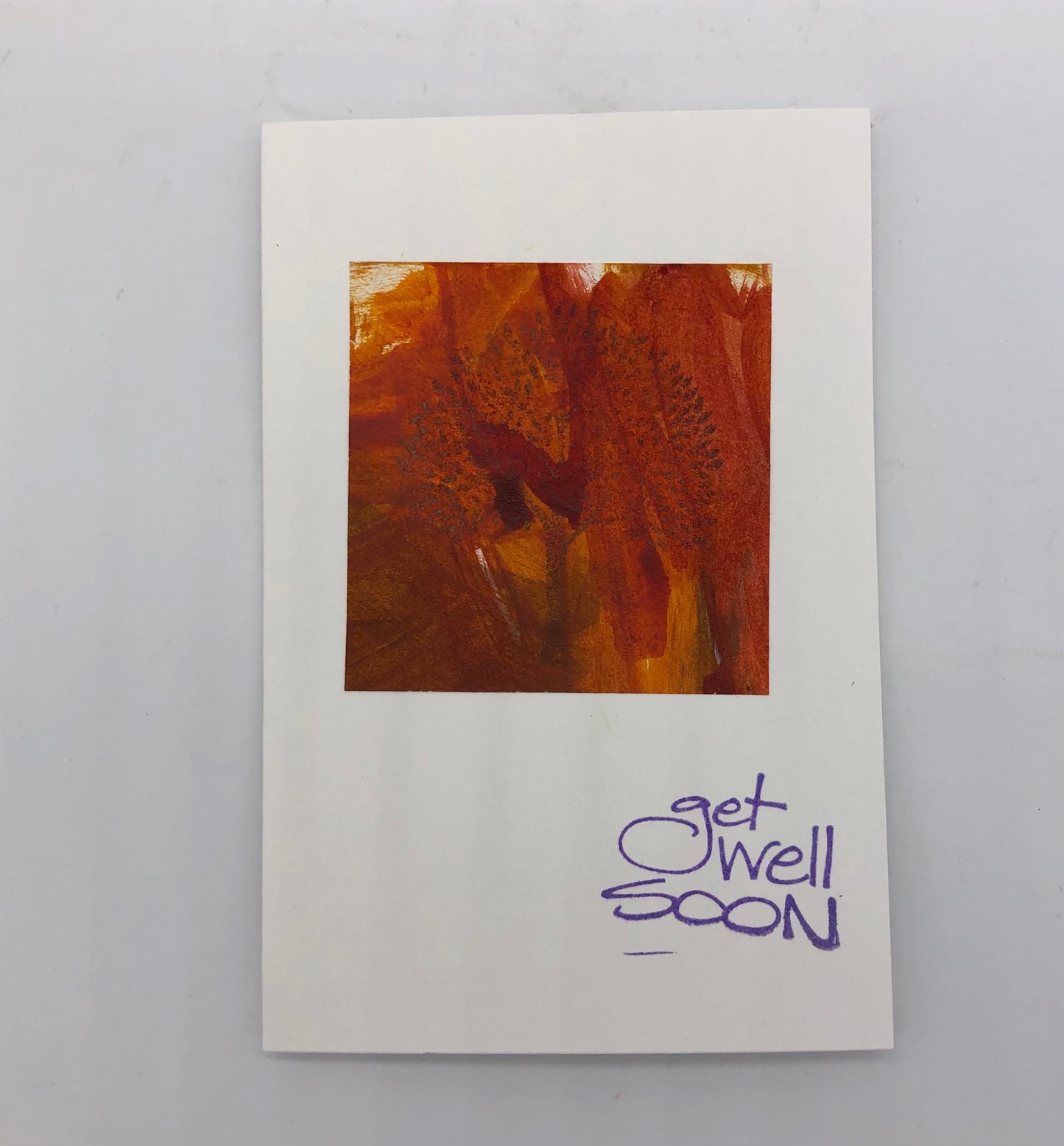 White greeting card with an orange painting in a square taking up about half.  On the lower right hand in purple Get Well Soon is stamped.