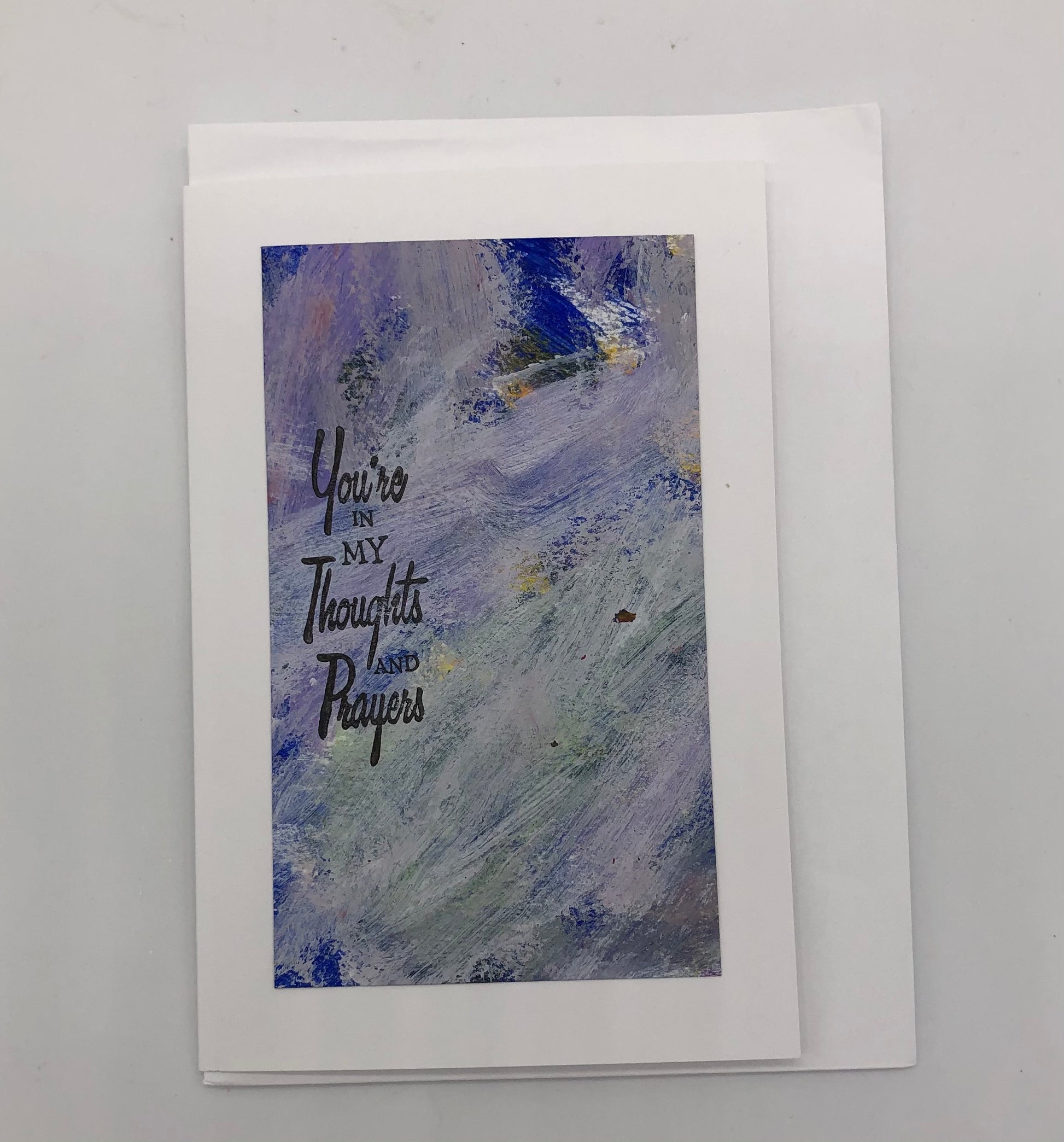 White greeting card with large acrylic painting in white and purple.  On top of the painting is stamped "You're in my thoughts and prayers" in black on the left hand side.