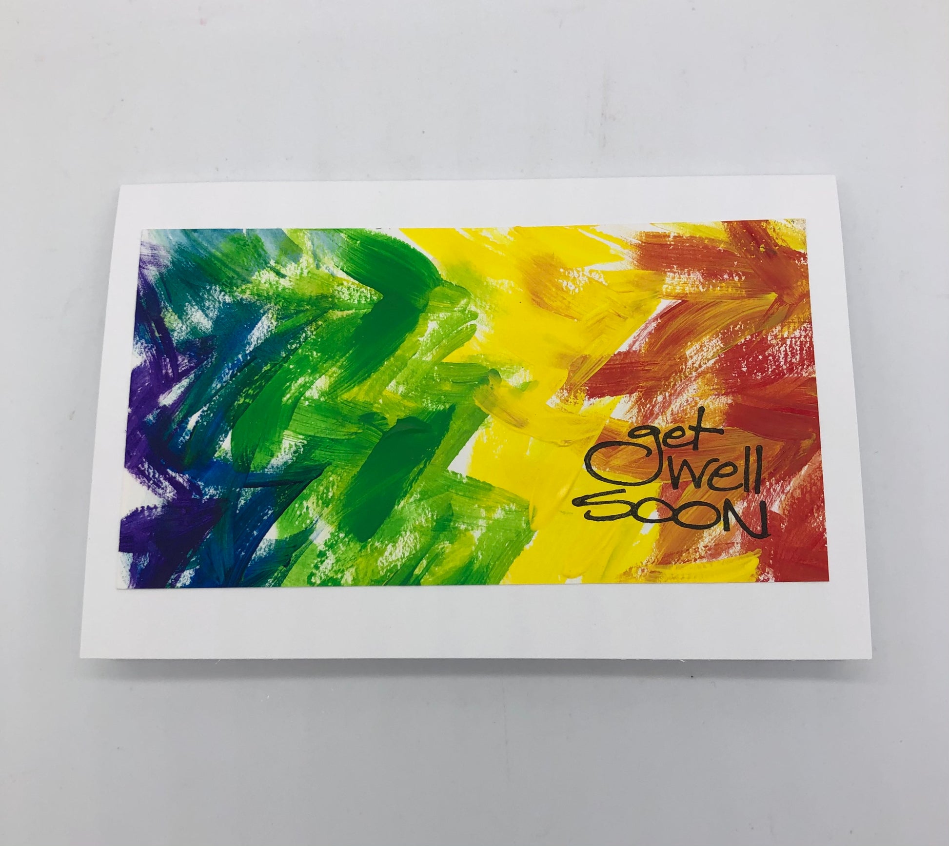 White greeting card with acrylic painting.  Painting is rainbow colors in vertical chevron design, with red on the right, then orange, yellow, green, blue and purple.  On top of the painted design it says get well soon in a black stamp.