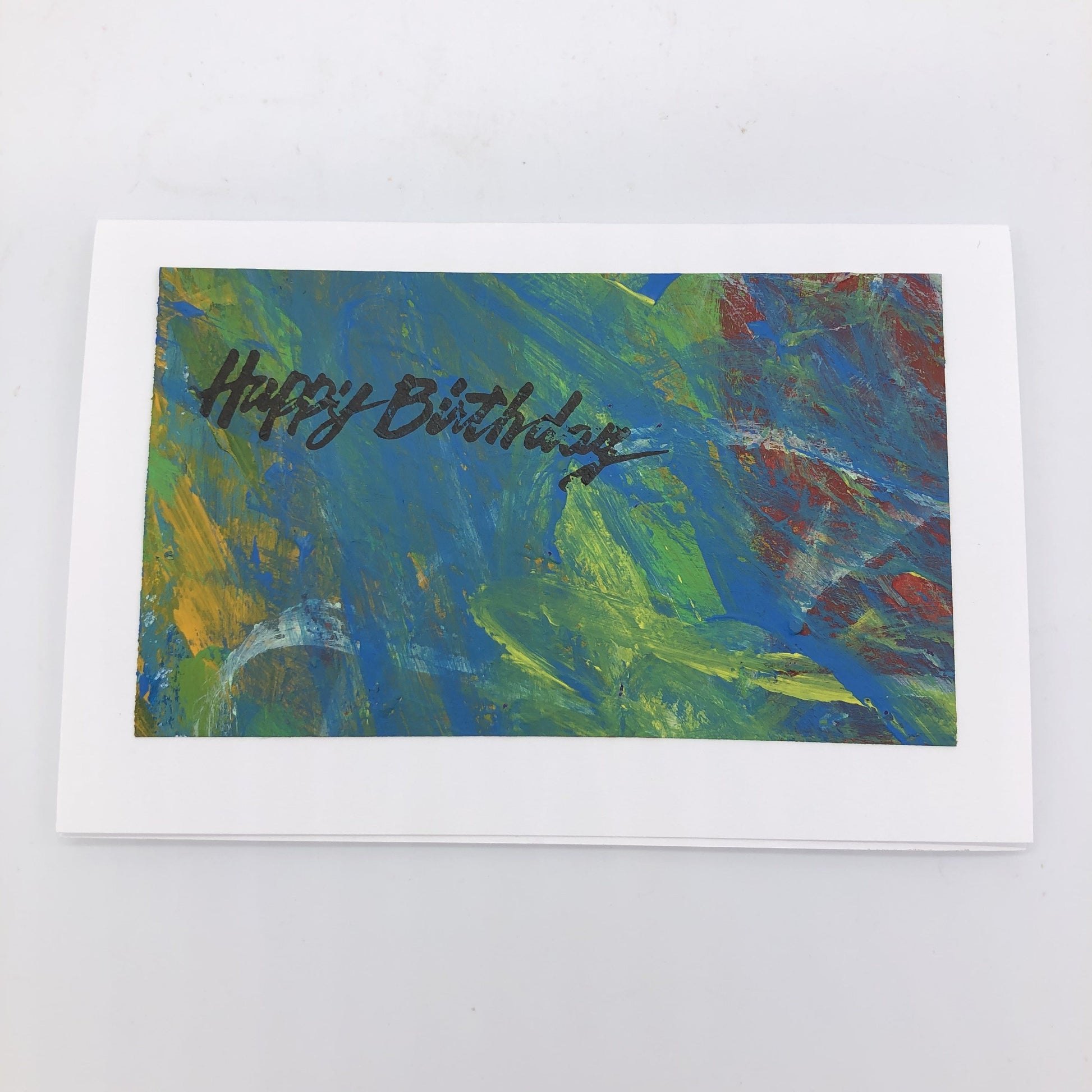 Handpainted acrylic background in mostly in bright blue, yellow a little red and some white.  On top of it in the upper left hand corner in a script font it says Happy Birthday in black type.