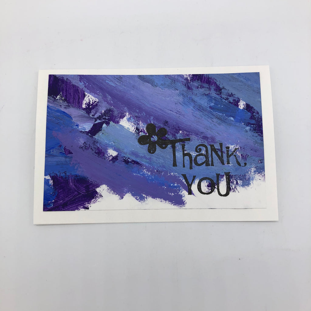 White greeting card with paint strokes in purple, shite and blue.  On top is a stamp that says thank you with a simple flower on the T