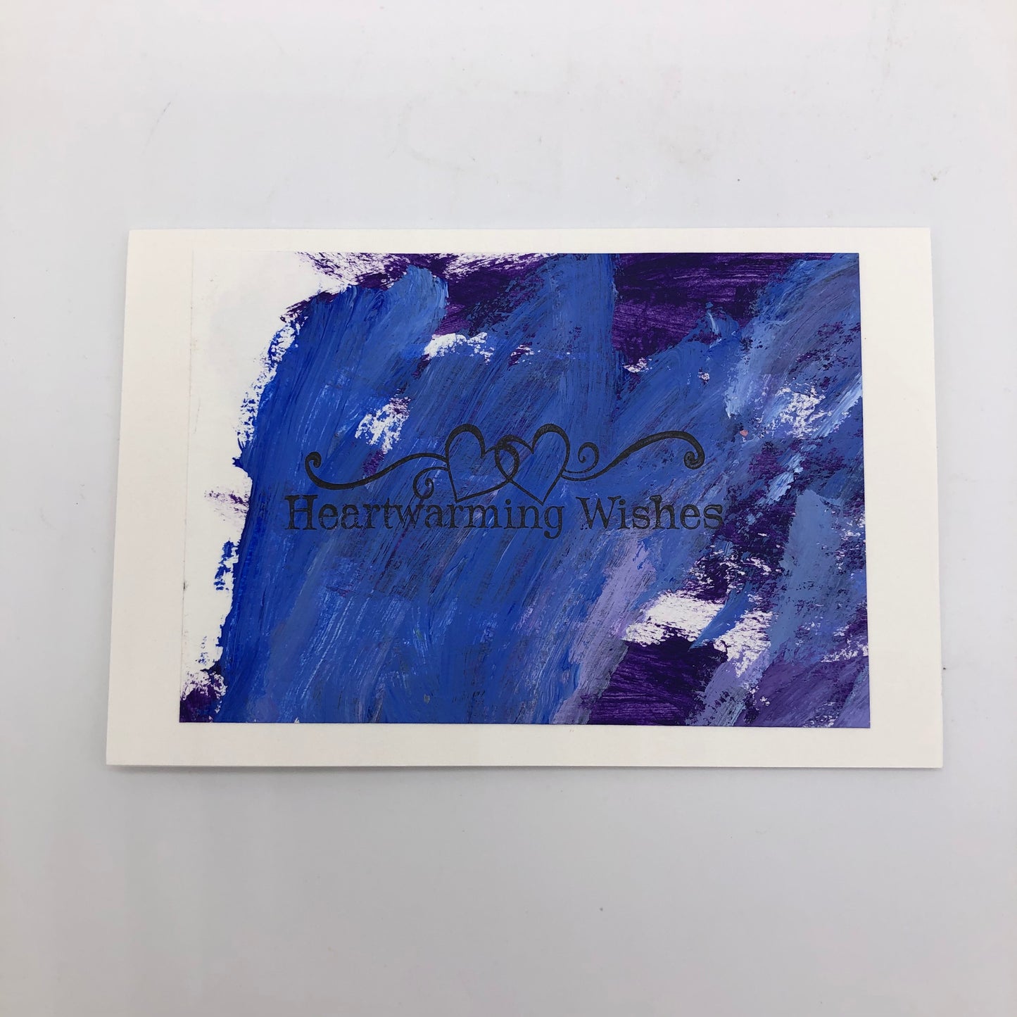 White greeting card with purple acrylic painted on top.  THere is a stamp that says "Heartwarming wishes in the middle and two outline hearts with flourishes to either side.